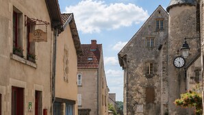 A narrow street with stone buildings, a clock, and a sign reading 'Gîte'. - Medieval house in Berry with private courtyard and all-inclusive (Saint-Benoît-du-Sault)