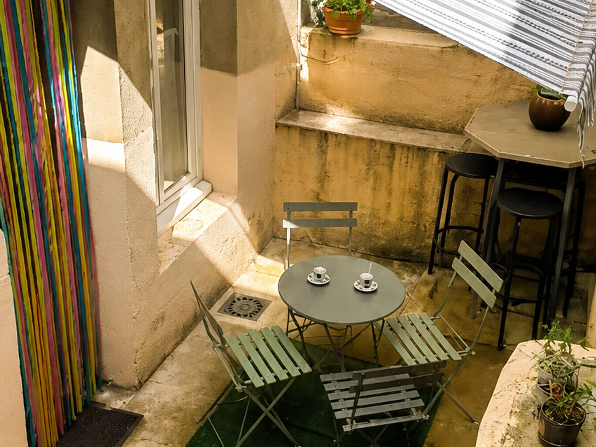 Un pequeño patio al aire libre con una mesa, sillas, una ventana y una maceta.
