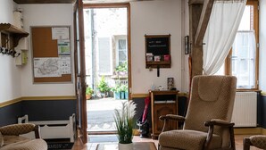 A room with a wooden chair, a sofa, a coffee table, a bulletin board, and a view of the street outside. - Medieval house in Berry with private courtyard and all-inclusive (Saint-Benoît-du-Sault)
