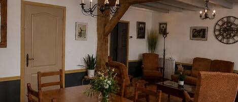 A dining area with a wooden table, chairs, a vase of flowers, a chandelier, and a clock on the wall.