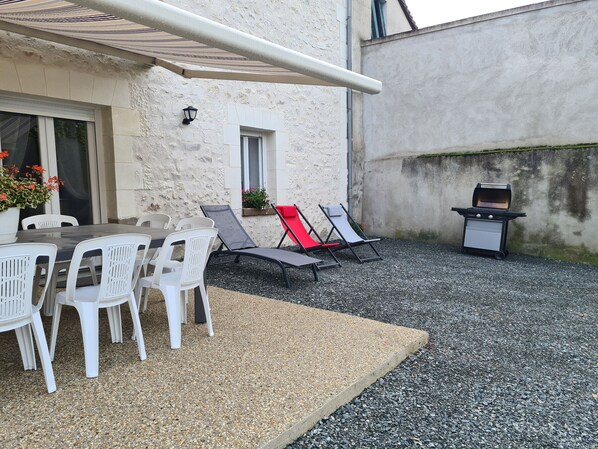 An outdoor patio with a table and chairs, a barbecue grill, and a shaded area. - Family cottage near Beauval Zoo with private courtyard (Lye)