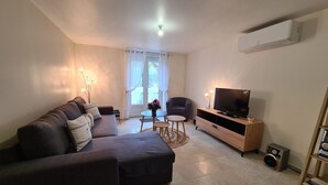 Ein Wohnzimmer mit einem dunkelgrauen Sofa, einer Holz-TV-Konsole, einem kleinen runden Tisch und einem Sessel.
