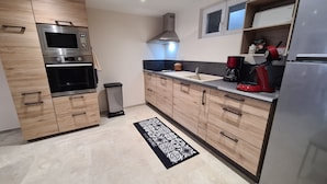 Eine moderne Küche mit Holzschränken, Edelstahlgeräten, einem schwarzen Mülleimer und einem gemusterten Teppich.