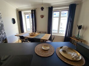 A dining area with a table set for two, a window with curtains, and a small side table with a vase. - Comfortable apartment for 4 in Épinal with private parking (Épinal)