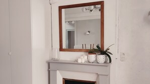 Une pièce avec une cheminée blanche, un miroir au-dessus et une petite étag ère ornée de bougies et d’une plante.