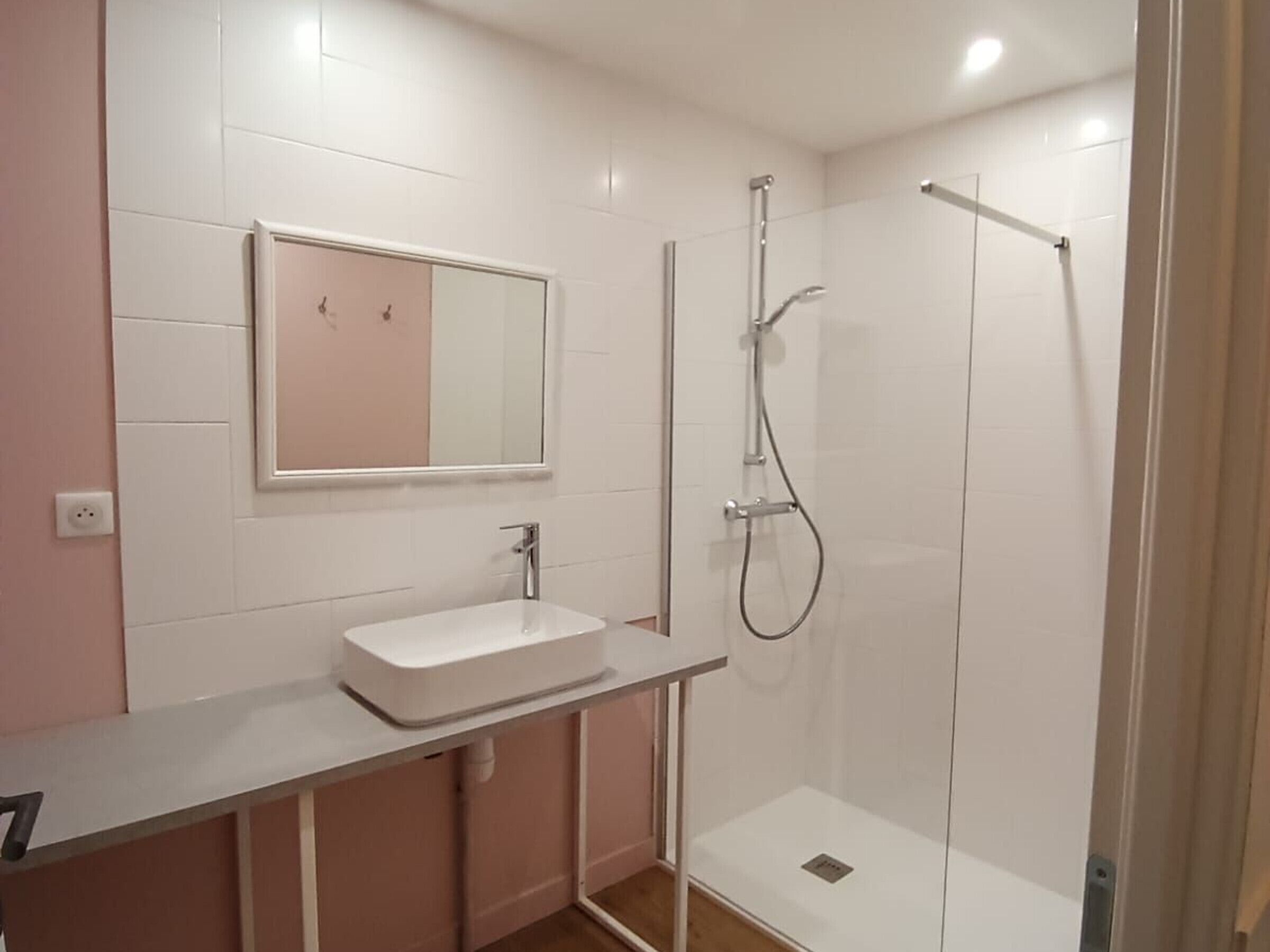 Une salle de bain avec un lavabo blanc, un miroir et une douche.