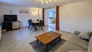 Ein Wohnzimmer mit Fernseher, Esstisch, Stühlen, einer Couch und einem Couchtisch.
