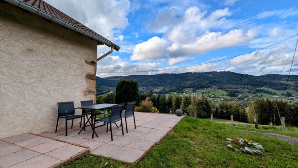 Eine Terrasse mit Gartenmöbeln, einer Steinmauer und Blick auf ein Tal mit Bergen.