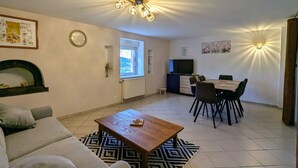 Ein Wohnzimmer mit Sofa, Couchtisch, Kamin, Essbereich mit Tisch und Stühlen sowie Fernseher.