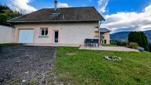 Ein zweigeschossiges Haus mit Ziegeldach, Garage und kleiner Terrasse mit Sitzgelegenheiten.