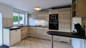 Eine moderne Küche mit hellen Holzschränken, einer schwarzen Arbeitsplatte, einem eingebauten Backofen und einer Pendelleuchte.