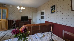 A dining area with a table set for two, a television, and a floral wallpaper pattern. - Charming farmhouse with garden near Lake Eguzon (Gournay)