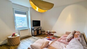 A modern bedroom with a large bed, a TV, and a view of the city through the window. - Renovated apartment with garden, parking, and WiFi in Gérardmer (Gérardmer)