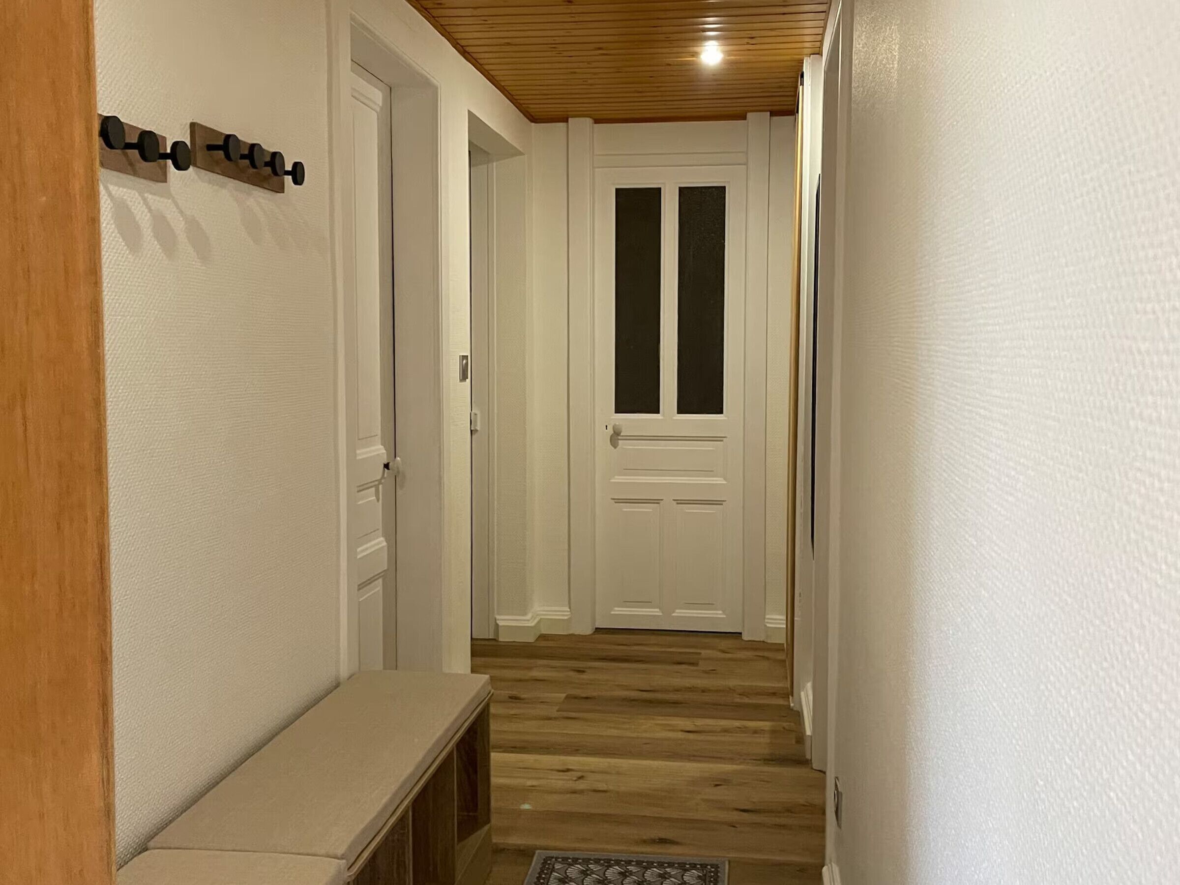 A hallway with a wooden bench, a white door with glass panels, and a ceiling with wooden beams.