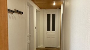 A hallway with a wooden bench, a white door with glass panels, and a ceiling with wooden beams. - Renovated apartment with garden, parking, and WiFi in Gérardmer (Gérardmer)