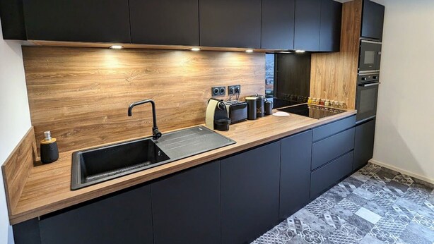 A modern kitchen with dark cabinetry, a wooden countertop, and built-in appliances. - Renovated apartment with garden, parking, and WiFi in Gérardmer (Gérardmer)