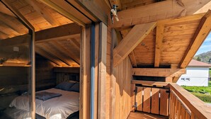 En træhytte med soveværelse på loftet, en balkon og udsigt over det omkringliggende landskab.