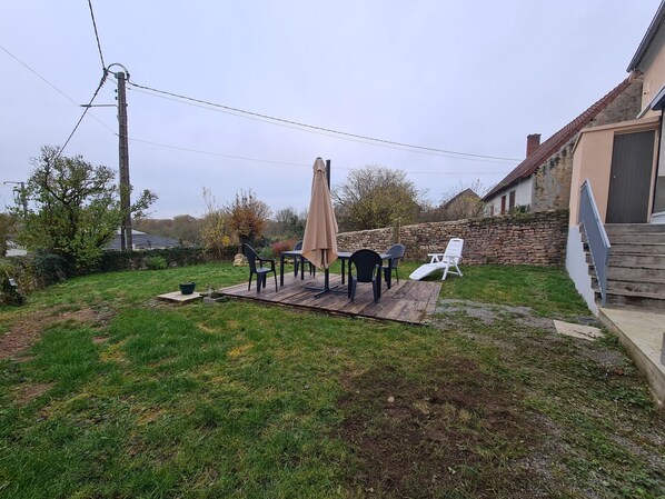 Un patio trasero con terraza de madera, mobiliario exterior y un muro de piedra.