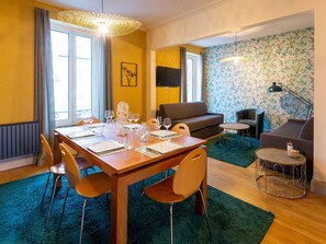 A dining area with a wooden table set for six, a sofa, a round coffee table, and a patterned wallpaper. - Elegant retreat in Nancy with 3 spacious bedrooms (Nancy)