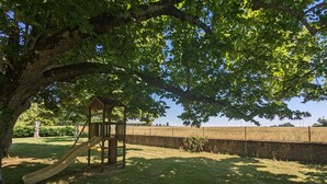A playground with a slide and a wooden playhouse under a large tree.