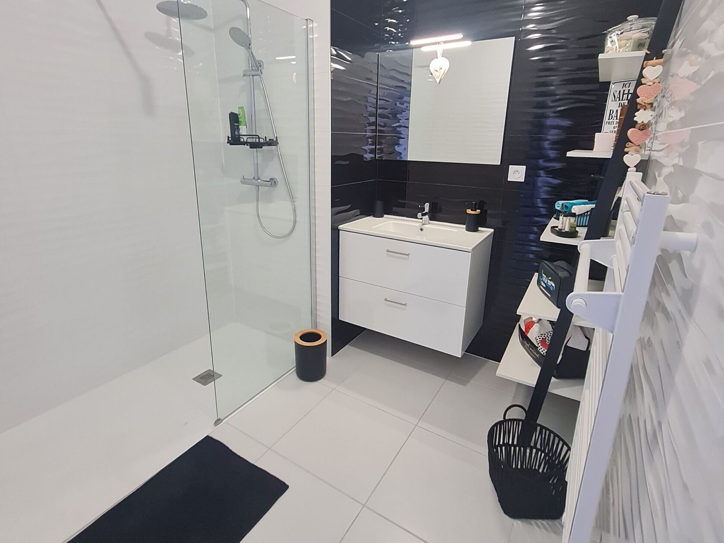Un baño moderno con cabina de ducha de vidrio, un lavabo blanco y un mueble de tocador blanco y negro.