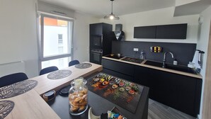 Une cuisine compacte avec un coin repas, dotée d’un design moderne avec des meubles de couleur noire, un four encastré et un petit îlot central muni d’un porte-épices.