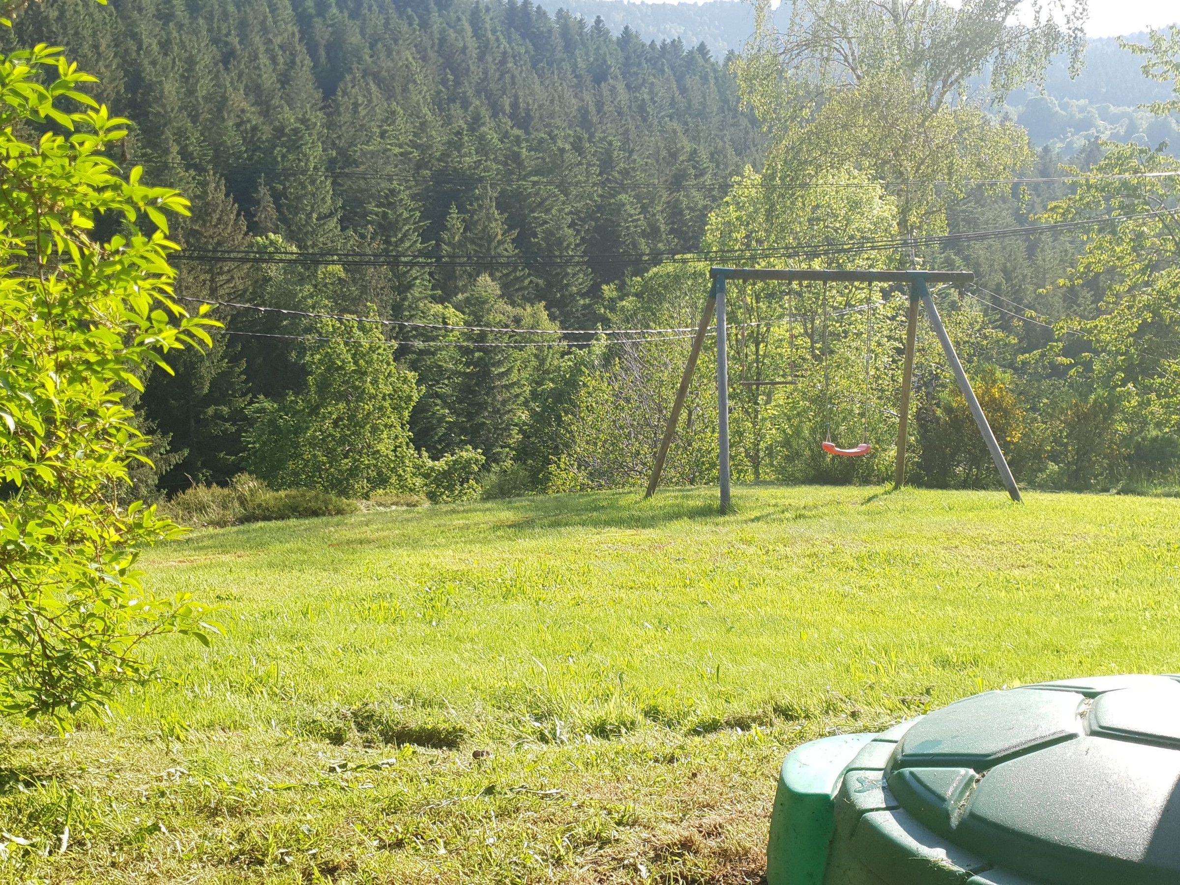 A grassy outdoor area with a swing set and a green object in the foreground.