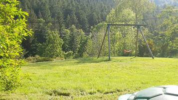 A grassy outdoor area with a swing set and a green object in the foreground.