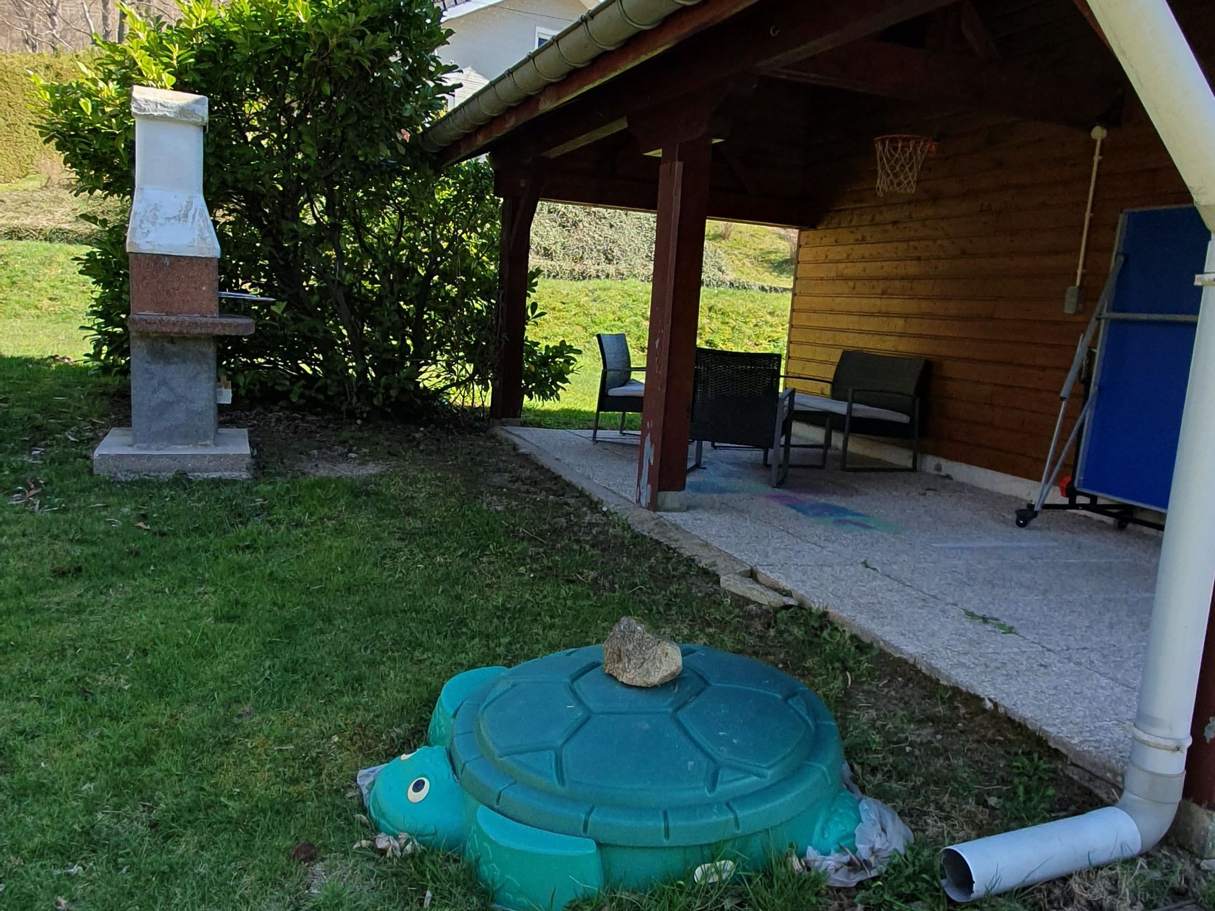 A covered outdoor area with a stone structure, a green turtle-shaped object, and a basketball hoop.