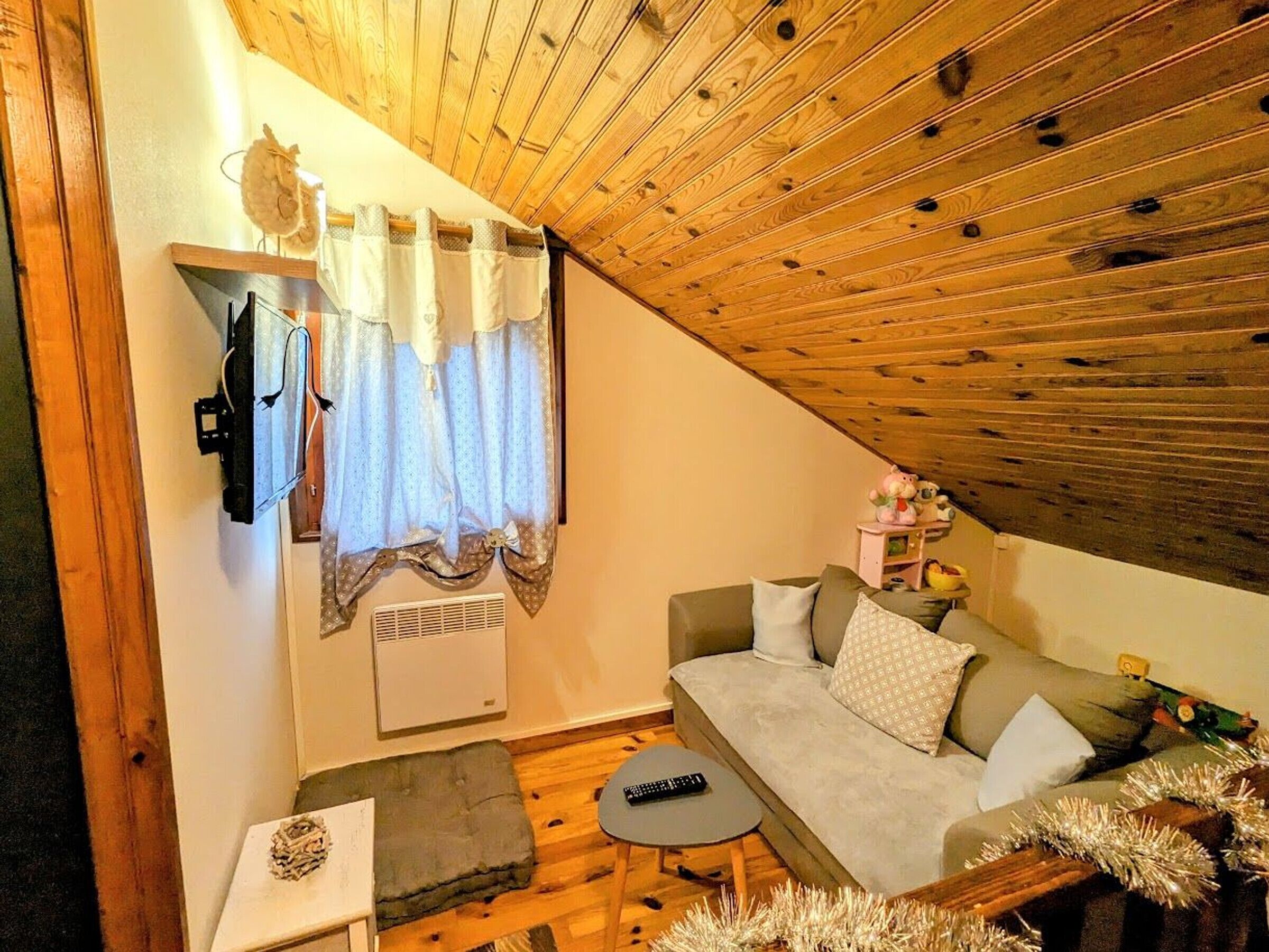 Ein gemütliches Wohnzimmer mit Holzboden, einer Couch, einem kleinen Tisch und einem Fenster mit Vorhängen.
