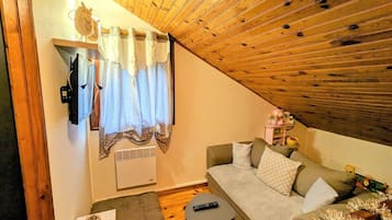 Ein gemütliches Wohnzimmer mit Holzboden, einer Couch, einem kleinen Tisch und einem Fenster mit Vorhängen.