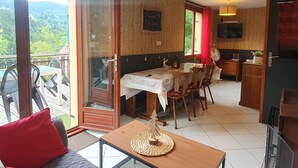 Una stanza con un tavolo da pranzo, sedie, un piccolo tavolino con sottovaso di vimini, un divano con cuscino rosso, una televisione e un mobiletto in legno.