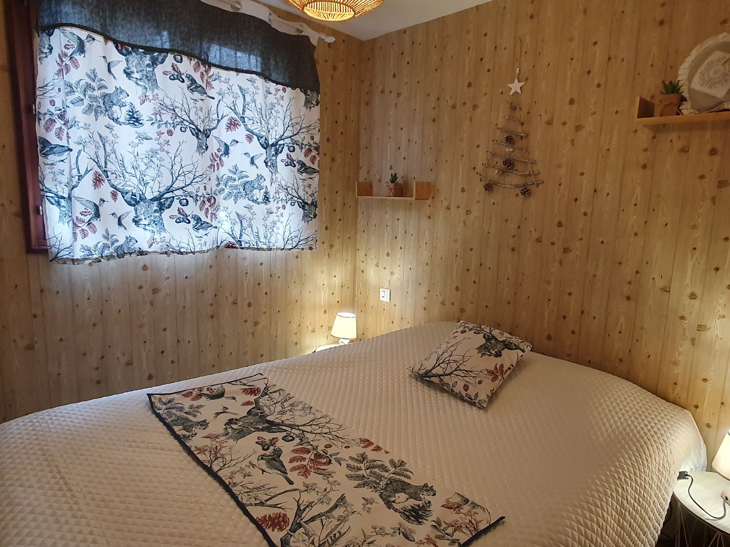 A bedroom with a bed, a window with a curtain, a bedside lamp, and a wall-mounted shelf.