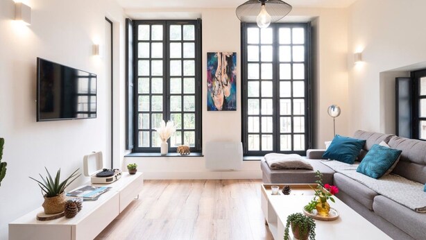Un salon moderne doté d’un téléviseur à écran plat, d’un canapé, d’une table basse et de grandes fenêtres.