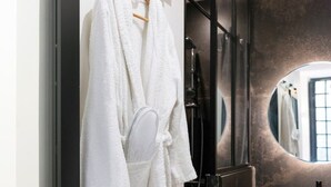 Une salle de bain moderne avec un peignoir blanc suspendu à un porte-serviettes en bois, un miroir rond et un lavabo noir doté d’un bac rond.