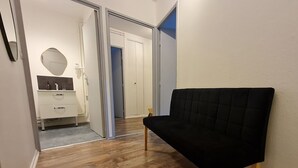 A hallway with wooden flooring, a black sofa, and a white dresser with a mirror. - Central and quiet apartment, near Stanislas Square (Nancy)