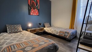 A hotel room with two beds, a desk with a lamp, a painting on the wall, and a window with curtains. - Central and quiet apartment, near Stanislas Square (Nancy)
