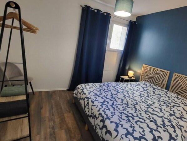 A bedroom with a patterned bedspread, a wooden ladder, a small bedside table with a lamp, and a window with curtains.