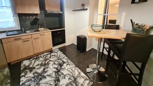 A modern kitchen with wooden cabinets, a built-in oven, a dining area with a high table and chairs, and a patterned rug. - Central and quiet apartment, near Stanislas Square (Nancy)