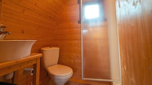 Baño de cabaña de madera con lavamanos, inodoro y cabina de ducha.