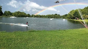 Una persona practicando wakeboard en un lago, con un arcoíris al fondo.