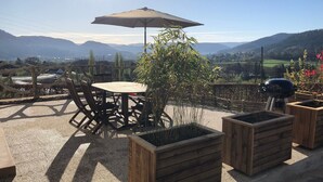 An outdoor patio with a round table and chairs, a wooden planter, and a barbecue grill. - Renovated house near Vosges, ideal for outdoor activities (Saint-Nabord)