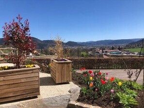 A garden with wooden planters and a variety of flowers, a wooden fence, and a view of a town and hills in the distance.