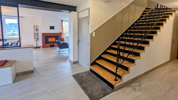 A modern interior with a wooden staircase, a fireplace, and a view through a window. - Renovated house near Vosges, ideal for outdoor activities (Saint-Nabord)