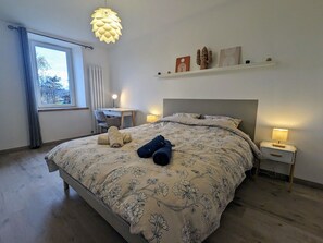 A bedroom with a bed, bedside tables, a desk, and a hanging light fixture.