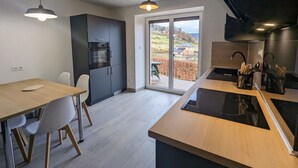 A modern kitchen with a dining area, a built-in oven, and a large sliding glass door leading to a balcony. - Renovated house near Vosges, ideal for outdoor activities (Saint-Nabord)