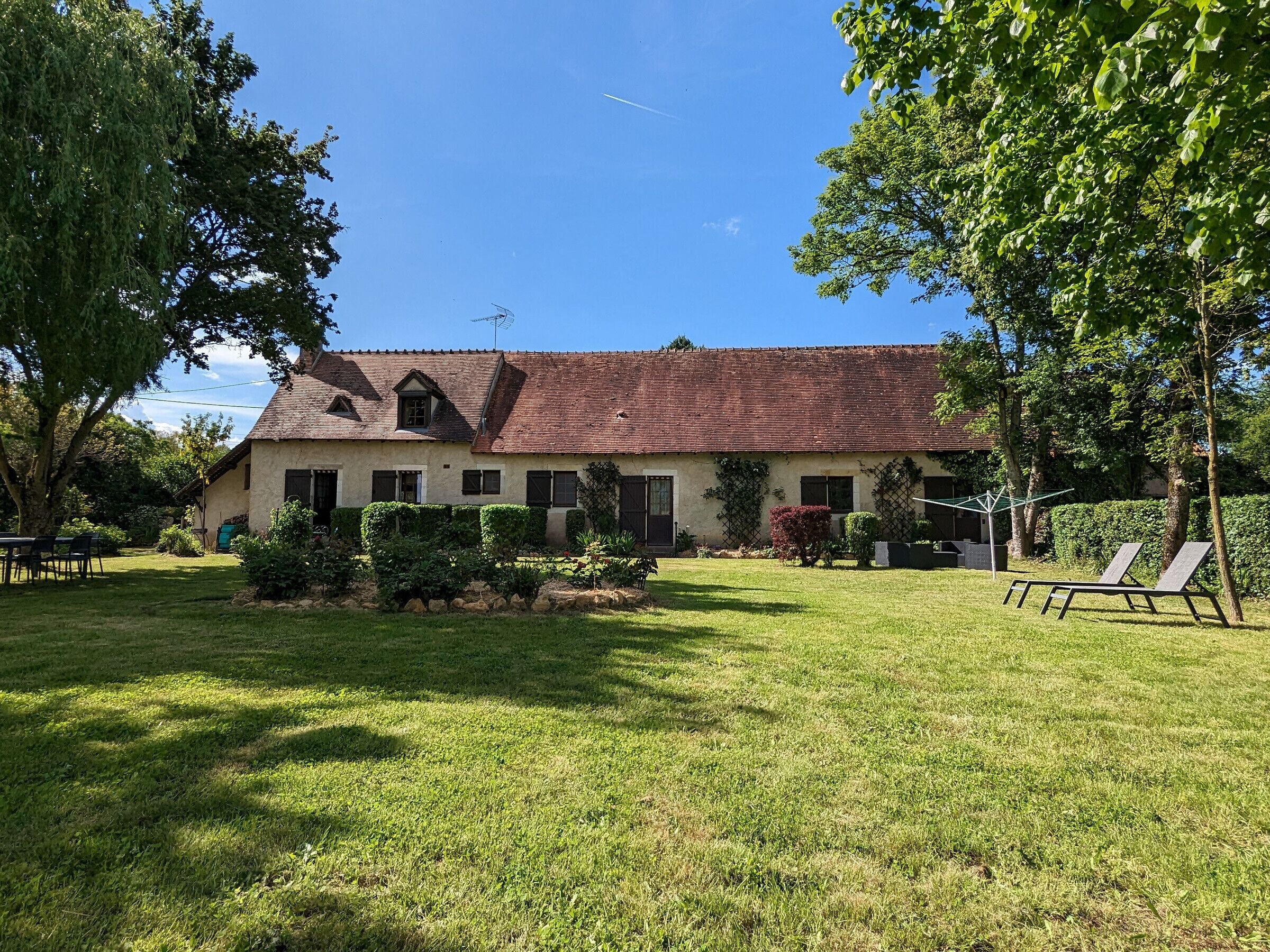 A two-story house with a red-tiled roof, surrounded by a well-maintained lawn and several trees.