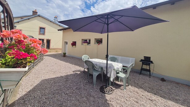 Une terrasse extérieure avec une table et des chaises, protégée par un grand parasol, et entourée de gravier et de plantes en pot.