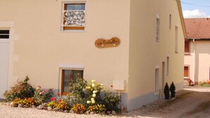 Un bâtiment à la façade beige, doté d’un toit en tuiles et d’un petit jardin où poussent différentes sortes de fleurs.