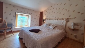 Une chambre à coucher avec un grand lit, une fenêtre donnant sur un beau paysage, un fauteuil et une table de chevet avec une lampe.